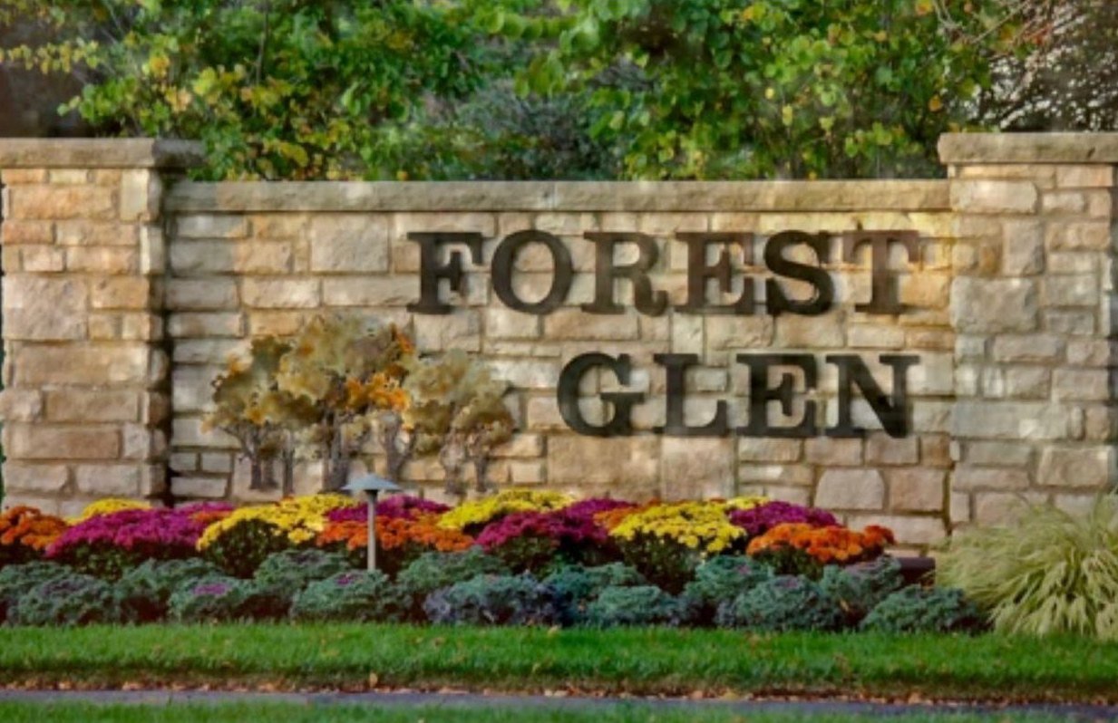 Forest Glen entrance monument in autumn, with a bed of orange, yellow, and burgundy mums at its base