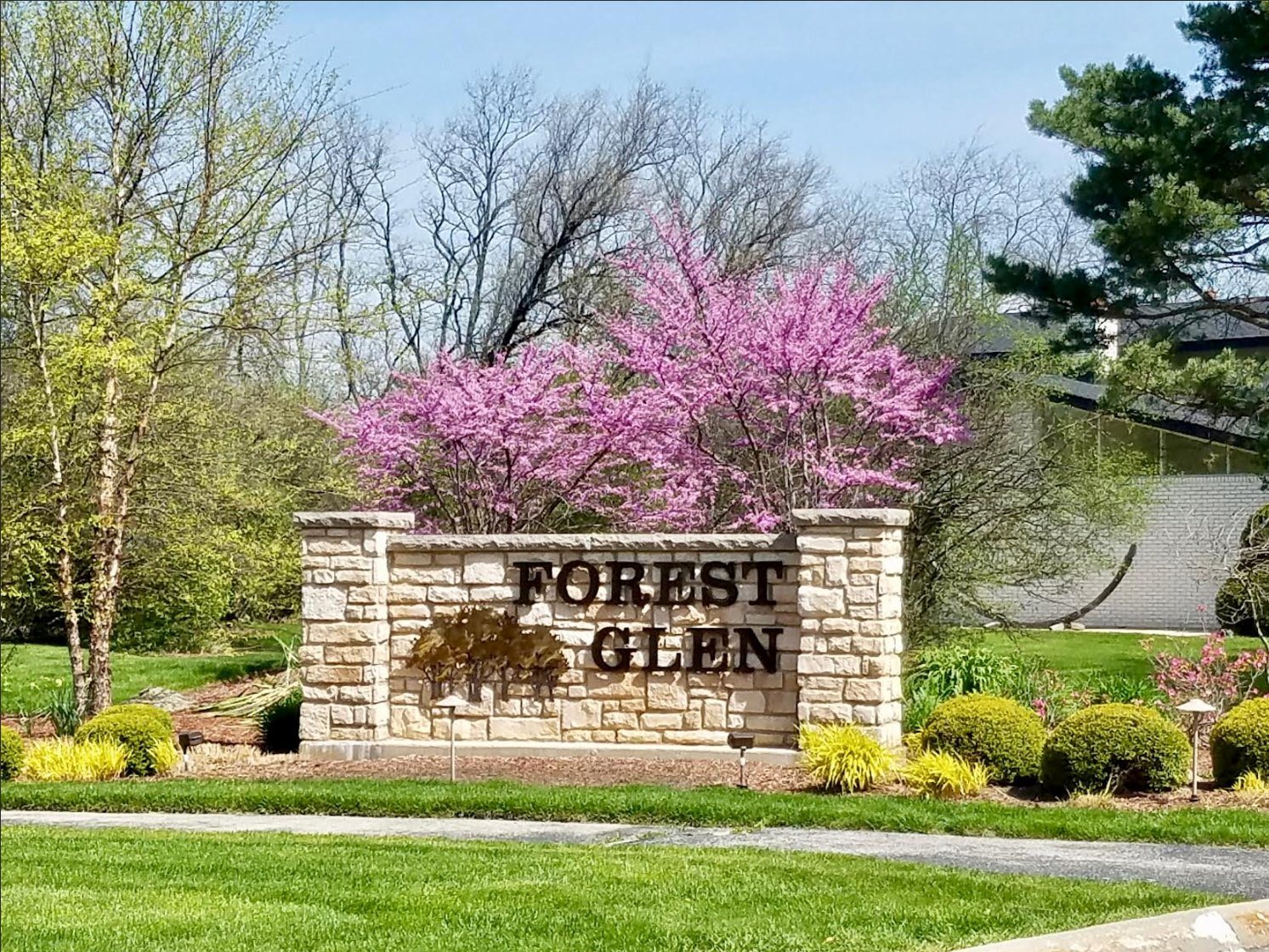 Forest Glen entrance monument in spring, with redbud trees in full pink bloom behind the limestone wall