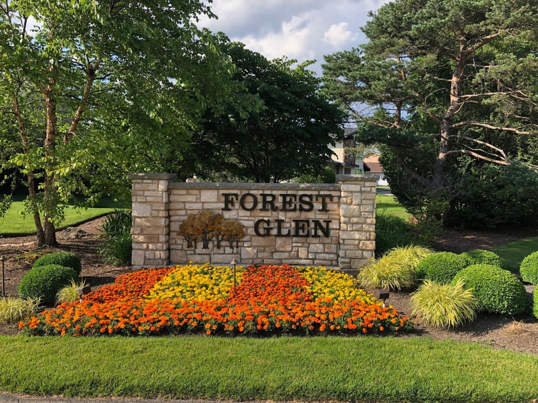 The Forest Glen limestone entrance monument in summer, with a bed of orange and yellow marigolds in full bloom at its base